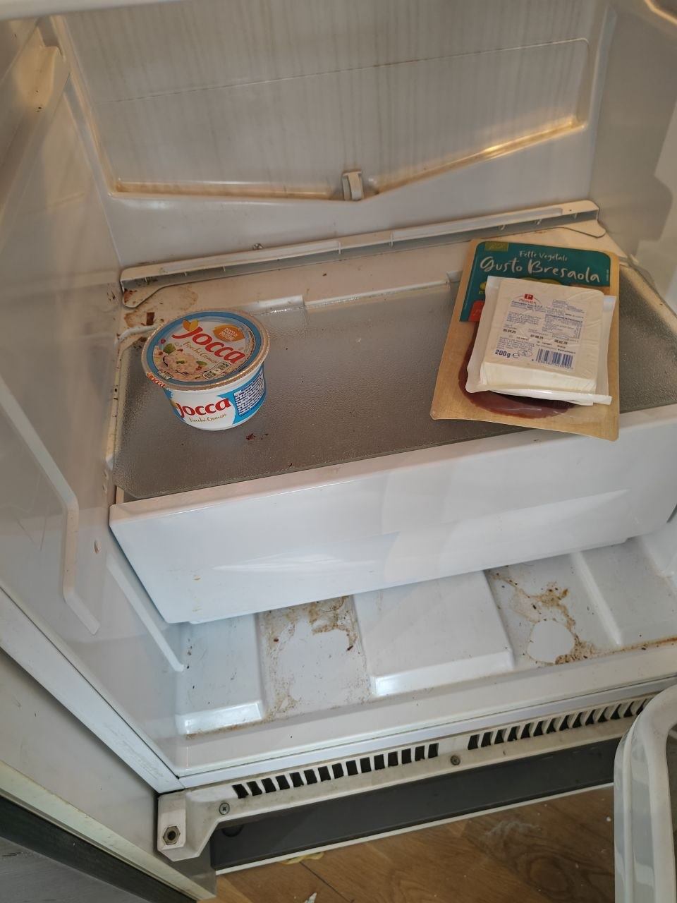 Interno del frigorifero con macchie e residui di cibo sul fondo e sui bordi